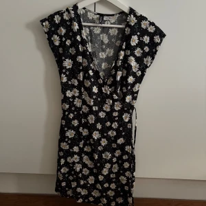 Svart blommig klänning - Supersöt svart klänning från Only med vita och gula blommor. Omlottmodell med knyt i midjan och v-ringning. Perfekt för sommarens alla tillfällen🌼