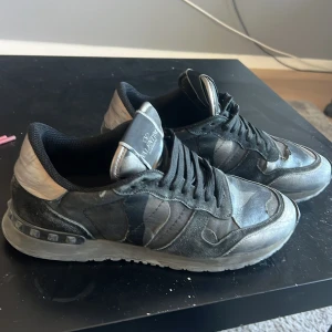 Valentino Garavani rockrunners 🤩 - Snygga sneakers från Valentino Garavani i svart och grått camouflagemönster. Skorna har svarta snören, rund tå och platt sula. Tillverkade i en mix av skinn och textil för en cool och urban look. Perfekta för dig som gillar streetstyle och exklusiva märken. Hör av er vid minsta fråga 😃 kan gå med i pris vid snabbt köp✅ byter hjärna också