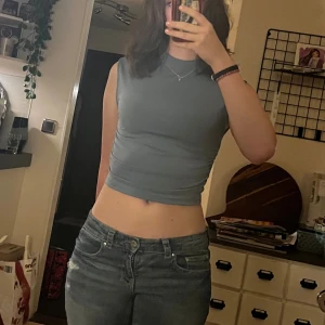 Ljusblå  croppad ärmlös topp - Säljer en ljusblå croppad topp med hög hals och ärmlös design. Toppen har en tight passform och är tillverkad i ett mjukt, stretchigt material som sitter snyggt mot kroppen. Storlek S.