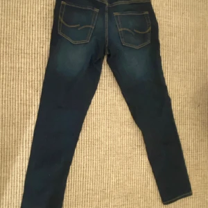 Jack & Jones blå jeans  - Mörkblå jeans från Jack & Jones i storlek 158, med snygga slitningar och kontrastsömmar. Modellen är slim fit med klassiska bakfickor och raka ben. Perfekta för dig som gillar en stilren och enkel look.