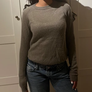 Grå stickad tröja med rund hals - Mysig brun stickad tröja med rund halsringning och långa ärmar. Enkel och stilren modell som passar perfekt till jeans eller kjol. Tröjan har en normal passform och är superbekväm för kyligare dagar.