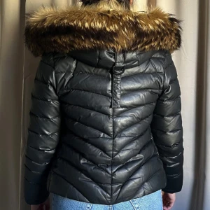 Svart pufferjacka  - Snygg svart pufferjacka med fluffig ÄKTA päls på huvan. Jackan har quiltad design, dragkedja framtill och två fickor med dragkedjor. Perfekt för kalla dagar. Nypris 1999kr