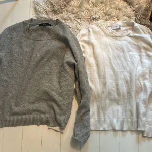 Grå och vit stickad tröja från VILA - Två stickade tröjor i klassisk modell, en i ljusgrått och en i vitt från VILA. Båda har rund halsringning, ribbade muddar och lång ärm. Perfekta för lager-på-lager och chill dagar. Snygga till jeans eller kjol. Köp en för 150kr eller båda för 250kr