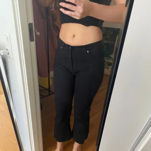 Svarta croppade byxor från Ober - Säljer ett par svarta byxor från Ober i modell Espiegle. Byxorna är croppade med lätt utsvängda ben och hög midja. Klassisk femficksdesign och stängs med knapp och dragkedja. Perfekta till sneakers eller boots.