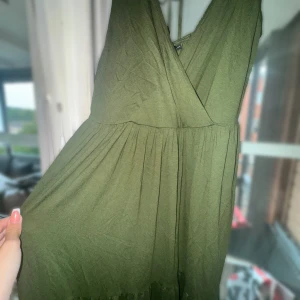 Olivgrön omlottklänning från Bodyflirt - Supersöt olivgrön klänning från Bodyflirt med omlottliv och virkade axelband. Klänningen har en flowy passform, knyt i nacken och v-ringning framtill. Perfekt för dig som gillar boho-vibes och vill ha något bekvämt men ändå snyggt.