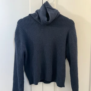 Mörkblå ribbad polotröja - Mysig mörkblå polotröja med ribbat stickat material och lång ärm. Tröjan har en hög polokrage! Den är kroppad.