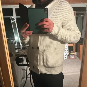 Calvin Klein- Kofta, Cardigan - Calvin Klein- Kofta, Cardigan Grovt texturerad stickning "fisherman's rib, Off-White / Kräm vit -Material: 60% bomull och 40% akryl, en blandning vilket gör den både mjuk och slitstark -Storlek: L (Large) -Skick: Mycket gott skick, väl omhändertagen, utan anmärkningar (se bilder).  Om du är intresserad av mått eller har andra frågor och funderingar- Skriv!