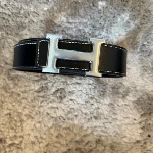 H-ermes Bälte  - Exklusivt och stilrent H-bälte i svart läder med vit kontrastsöm. En tidlös accessoar som lyfter varje outfit – perfekt både till vardag och mer uppklädda tillfällen.  ♦️ Svart läder med white stitching ☑️ ⚜️ Ikonisk H-detalj ☑️ ♦️ Elegant & mångsidig design ☑️  📦 Snabb leverans & trygg affär 