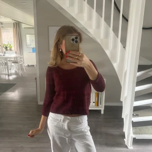 Vinröd stickad tröja med öppen rygg - Vinröd stickad tröja med trekvartsärm och snygg öppen rygg. Modellen är croppad och har en rund halsringning. Perfekt för dig som vill ha en trendig och unik look med lite extra edge.