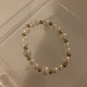 Pärlarmband med guldfärgade detaljer - Snyggt armband med vita pärlor i olika storlekar och små guldfärgade kulor mellan varje pärla. Perfekt för dig som gillar klassisk och elegant stil med en touch av lyx. Stretchig design som passar de flesta handleder.
