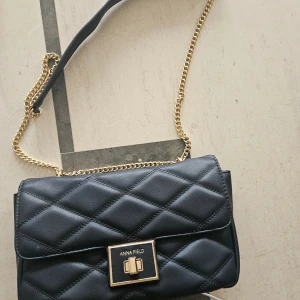 Svart quiltad axelväska Anna Field - Snygg svart axelväska från Anna Field med quiltad design och guldfärgad kedja. Väskan har ett elegant lås framtill och mjukt syntetmaterial. Perfekt storlek för det viktigaste och har en innerficka med logotyp. Stilren och trendig look.