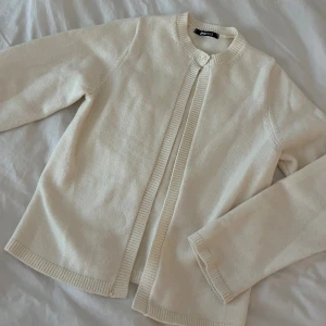 Krämvit kofta från Gina Tricot XS - Superfin krämvit kofta från Gina Tricot i storlek XS. Koftan är stickad med ribbade kanter och har en enkel, stilren design med rund halsringning och knapp upptill. Perfekt att slänga över en topp när det blir kyligt.