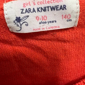 Röd croppad kofta från Zara Knitwear - Croppad röd kofta från Zara Knitwear med långa ärmar och knappar framtill. Dekorerad med en söt tygblomma på ena sidan. Tillverkad i mjuk stickad bomull, perfekt för lager-på-lager och snygg till jeans eller kjol.