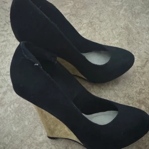 Svarta pumps med klack  - Snygga svarta pumps med hög klack i spegel form. Skorna har rund tå och är klädda i mockaliknande material. Perfekta för dig som vill ha både höjd och stabilitet i din look.