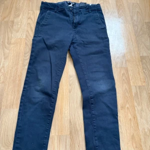 Mörkblå chinos från Cropp - Snygga mörkblå chinos från Cropp med raka ben och klassisk passform. Byxorna har sidfickor fram och två bakfickor med knappdetalj. Tillverkade i mjuk bomull med lite stretch för extra komfort. Perfekta för en clean och stilren look.