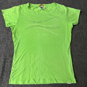 Grön t-shirt från The North Face - Snygg grön t-shirt från The North Face med diskret tryck framtill i form av vågiga linjer och text. Klassisk rund halsringning och korta ärmar. Tillverkad i mjuk bomull som känns skön mot huden. Perfekt för en avslappnad och sportig stil.