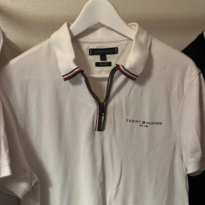 Vit pikétröja Tommy Hilfiger M - Vit pikétröja från Tommy Hilfiger i regular fit. Tröjan har dragkedja framtill och klassisk krage med röd, vit och marinblå randig detalj. Broderad logga på bröstet. Perfekt för en clean och sportig stil.