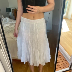 Vit långkjol från Tally Weijl - Superfin vit långkjol från Tally Weijl i lätt och flowigt material. Kjolen har subtila glittriga ränder och en vågig, luftig form som ger en snygg siluett. Perfekt för varma dagar när du vill känna dig både bekväm och stylish.