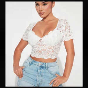 Vit spetsig croppad blus med v-ringning - Säljer en vit croppad blus i spets med v-ringning och korta ärmar. Blusen har ett blommigt spetsmönster och är figurnära med snygg passform. Perfekt att styla med jeans eller kjol för en trendig look.
