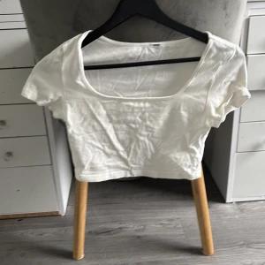 Vit croppad topp med kort ärm - Snygg vit croppad topp med korta ärmar och fyrkantig urringning. Perfekt att matcha med höga jeans eller kjol för en clean look. Tunn och mjuk i materialet, passar till alla säsonger.