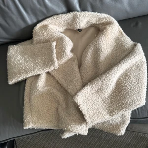 Beige teddyjacka med krage - Mysig och trendig beige teddyjacka med stor krage och knäppning framtill, men också med fickor. 