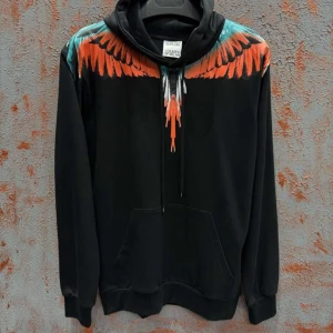  Marcelo Burlon hoodie - Svart hoodie från Marcelo Burlon med ikoniskt vingmönster i orange, turkos och vitt över axlar och bröst. Tröjan har huva med snörning och en stor magficka. Perfekt för dig som vill sticka ut med en unik streetstyle.