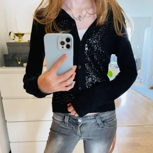 Svart kofta med paljetter - Svart kofta med knappar framtill och glittriga paljetter på framsidan från H&M. Långärmad och figurnära modell som ger en snygg och stilren look.