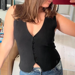 Topp med knappar - Svart stickad väst med knappar framtill