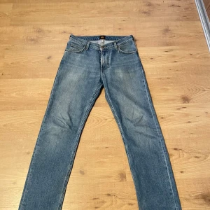 Blå raka jeans från Lee - Klassiska blå jeans från Lee med rak passform och fem fickor. Jeansen har en snygg mellanblå tvätt och Lee-logga på bakfickan. Tillverkade i slitstarkt denimtyg som ger en tidlös look. Perfekta för dig som gillar enkel och stilren stil.