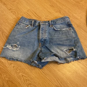 Blå jeansshorts från g perfect jeans - Snygga blå jeansshorts från g perfect jeans i klassisk modell med hög midja. Shortsen har slitna detaljer, råa kanter och fem fickor. Perfekta för en chill sommarlook och passar till allt. Materialet är 100% denim och färgen är mellanblå.