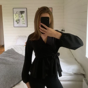 Svart omlottblus från Missay - Svart omlottblus med v-ringning och knyt i midjan från Missay. Blusen har långa, lätt puffiga ärmar med resår vid handlederna och ett flowy fall nedtill. Perfekt för dig som gillar stilrena och trendiga plagg. Säljer då den ibte kommer till användning! 💋om du undrar över något så fråga bara. 