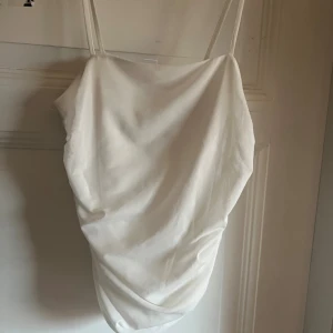 Vit omlotttröja Gina Tricot - Supersnygg vit tröja från Gina Tricot med tunna axelband och draperad omlott-effekt. Tröjan har en lätt glansig yta och är gjord i ett tunt, mjukt material som känns lyxigt. Perfekt för dig som gillar stilrena och trendiga plagg.