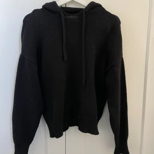Svart stickad hoodie från Zara  - Mysig svart stickad hoodie med huva och dragsnören. Tröjan har långa ärmar och ribbade muddar vid ärmslut och nederkant. 