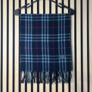 Rutig blå halsduk från Burberry - Snygg rutig halsduk från Burberry i marinblått med ljusblå och röda ränder. Gjord i 100% lammull och har klassiska fransar i ändarna. Perfekt accessoar för att lyfta din outfit med lite brittisk stil.  