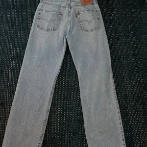 Levi's 565 ljusblå jeans W30 L32 - Ljusblå Levi's 565 jeans med loose fit och raka ben. Klassisk femficksmodell med Levi's läderpatch bak och röd etikett på bakfickan. Tillverkade i slitstarkt jeanstyg, perfekt för en avslappnad och trendig look.