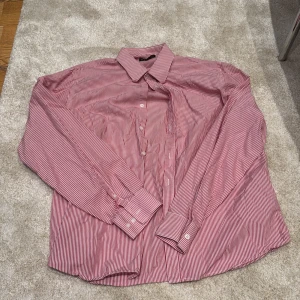 Rödvit randig skjorta från Murrey XL - Säljer en klassisk röd och vit randig skjorta från Murrey i storlek XL. Skjortan har långa ärmar, knappar framtill och vid manschetterna samt en snygg krage. Perfekt för dig som gillar stilrena och tidlösa plagg.