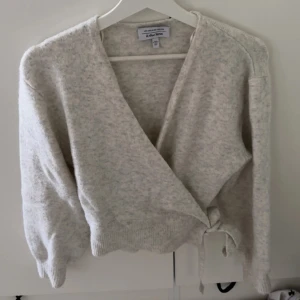 Ljusgrå omlottkofta från & Other Stories - Supermjuk ljusgrå omlottkofta från & Other Stories med knyt i sidan. Koftan har lång ärm, ribbade muddar och en loose fit som ger en chill vibe. Perfekt att slänga på sig över ett linne eller t-shirt för en avslappnad look.