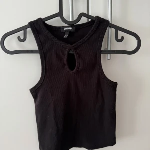 Svart ribbad linnetopp från DeFacto - Svart ribbad linnetopp från DeFacto med en snygg droppformad cut-out vid halsen. Toppen är ärmlös och har en tight passform som framhäver axlarna. Perfekt för dig som gillar minimalistisk och stilren design. Toppen är hel ny och är inte använt.