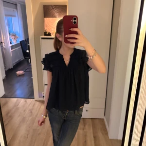 Mörkblå blus från Gina Tricot - Supersöt blus från Gina Tricot med volangdetaljer på axlarna och lätt v-ringning. Blusen är luftig och har små diskreta broderade prickar i tyget. Perfekt att styla med jeans eller kjol för en trendig look. I storlek 158/164.