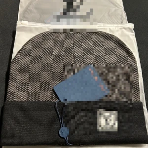 Svart och grå rutig mössa - Snygg mössa i svart och grått med rutigt mönster och uppvikt kant. Märkeslogga framtill och diskret design som passar perfekt till kalla dagar. Tillverkad i mjukt material för extra komfort.