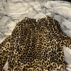 Leopardmönstrad blus från H&M - Snygg och flowy leopardmönstrad blus från H&M i storlek S. Skjortan har v-ringning och långa ärmar, perfekt för dig som vill sticka ut med ett djurmönster. Materialet känns lätt och luftigt, vilket gör den skön att bära.