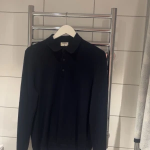 Mörkblå pikétröja från Filippa K - Klassisk mörkblå pikétröja från Filippa K med krage och knappar framtill. Tröjan är långärmad och har en stilren, minimalistisk design som passar perfekt till en clean och snygg look. Materialet känns mjukt och bekvämt mot huden. Nypris 1500 kr