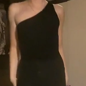 Svart oneshoulder body - Snygg svart body med oneshoulder-design och öppen rygg. Tight passform som framhäver figuren och ger en modern look. Perfekt för dig som vill sticka ut med en stilren och trendig outfit.