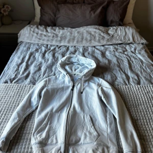 Vit hoodie från Jack & Jones - Säljer en stilren vit hoodie från Jack & Jones med dragkedja framtill och huva med snörning. Tröjan har två stora fickor och är tillverkad i mjuk bomull, perfekt för en avslappnad look. Skriv för fler bilder eller frågor. 