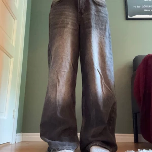 BDG baggy svarta jeans 24W 32L - Säljer ett par svarta jeans från BDG Urban Outfitters med breda ben och coolt tvättad look. Jeansen har klassisk femficksdesign, broderad logga på bakfickan och röda sömmar i midjan. Perfekt för dig som gillar loose fit och streetstyle.