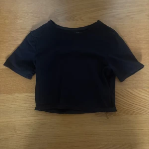 Svart croppad topp från 157 XS - En svart croppad topp från lager 157 i storlek XS. T-shirten har korta ärmar och rund halsringning. Tillverkad i mjuk bomull med lite stretch för en bekväm passform. Perfekt att matcha med höga jeans eller kjol.