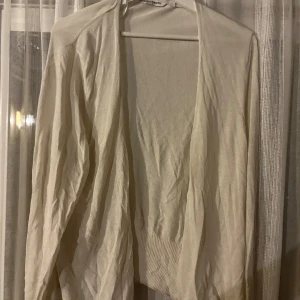 Beige kofta från KappAhl, stl L - Lätt och tunn beige kofta från KappAhl i storlek L. Öppen framtill utan knappar, med ribbad nederkant och långa ärmar. Perfekt att slänga över en topp för en chill och stilren look.