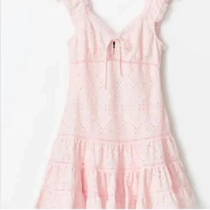 Ljusrosa volangklänning med spets - Supersöt ljusrosa kortklänning med volanger och broderad spets. Klänningen har v-ringning, knyt fram och är ärmlös med volangdetaljer vid axlarna. Perfekt för sommarens alla tillfällen!