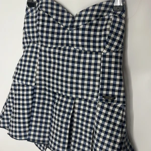 Rutig blåvit topp från Guess - Supersöt topp från Guess i blåvitt rutigt mönster. perfekt för att skapa en trendig look. Väldigt gullig och sommrig eller classy med dess volanger och hjärtformade över del.