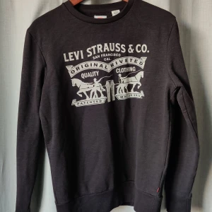 Svart sweatshirt från Levi's storlek S  - Svart sweatshirt från Levi's i bomull med klassiskt vitt tryck framtill. Rund hals, långa ärmar och ribbade muddar. Snygg och enkel design med ikoniskt Levi Strauss & Co. motiv. Perfekt för dig som gillar streetwear och vill ha en chill look. 
